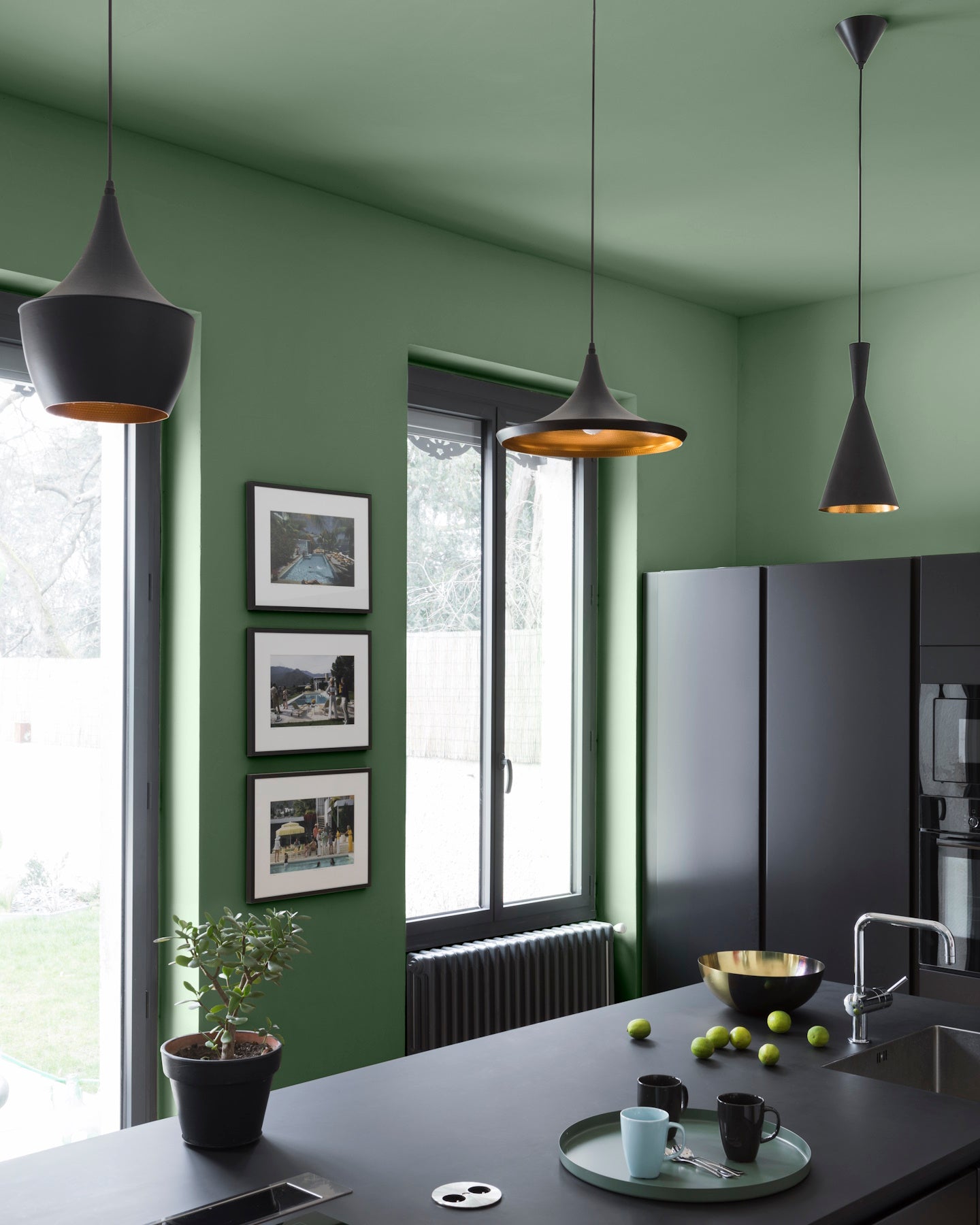 Cuisine ambiance moderne avec murs verts, peinture Velours de Peinture Vert Potager Libéron, avec cadres sur les murs, meubles, luminaires et électroménagers noirs.