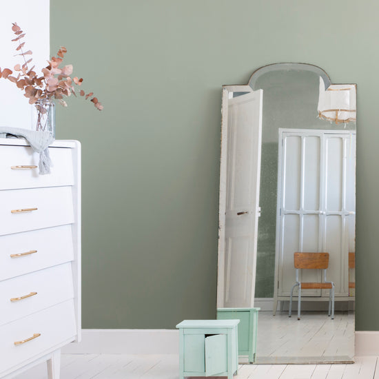 Chambre aux murs vert sauge et blanc meudon Libéron, avec commode blanche, miroir ancien et petit tabouret vert.