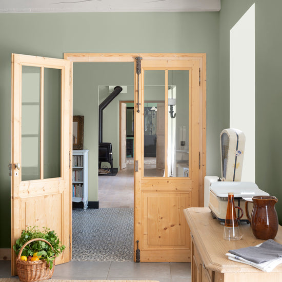 Cuisine aux murs vert sauge et crème topinambour Libéron, avec portes en bois clair, meuble en bois et panier végétal.