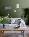 Salon lumineux avec murs verts, peinture Velours de Peinture Vert Treillis Libéron, canapé gris, bouquet de fleurs et table basse en bois.