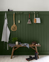 Entrée aux murs vert treillis et blanc grisaille Libéron, avec patères, banc en bois, bottes et accessoires suspendus.