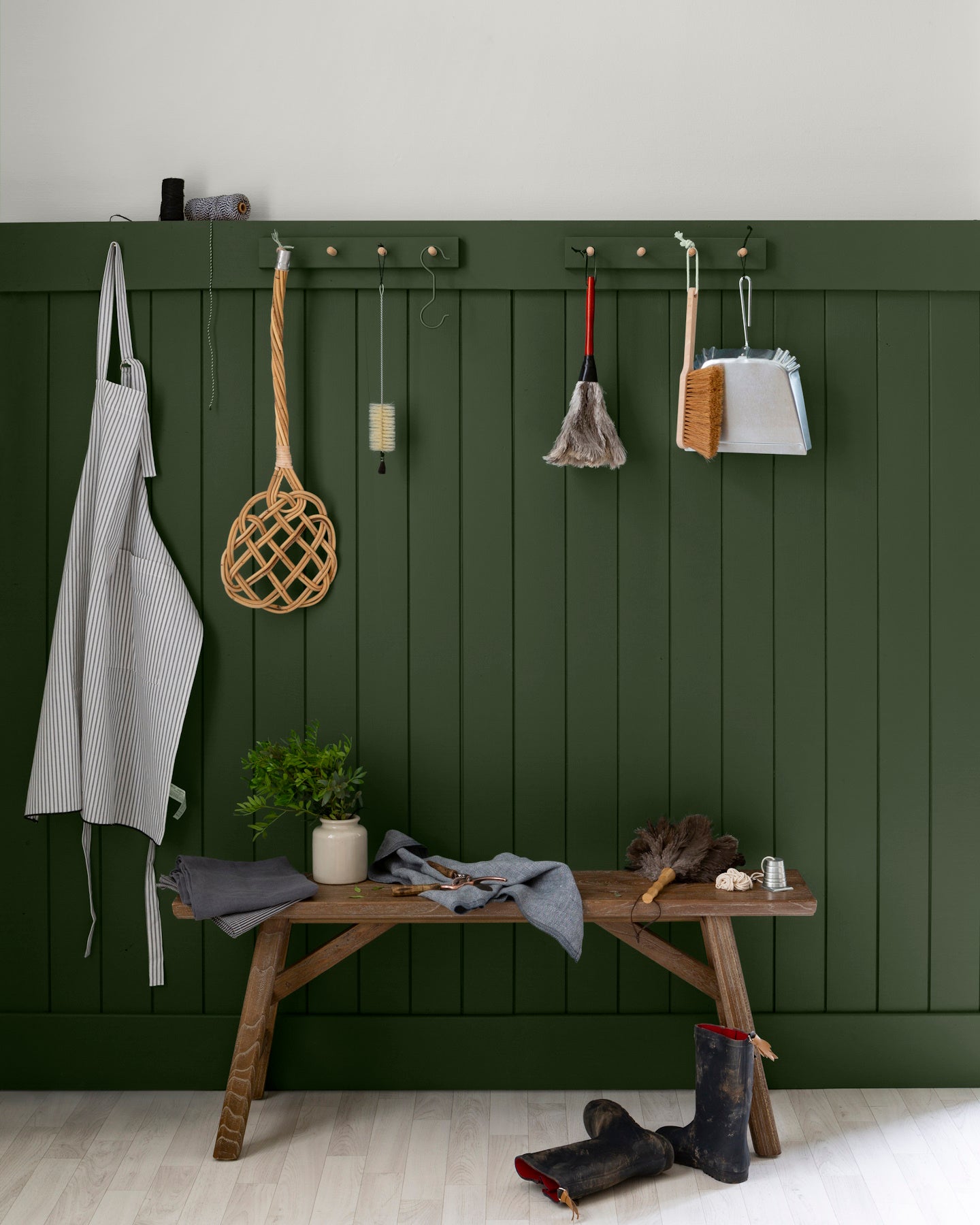 Entrée aux murs vert treillis et blanc grisaille Libéron, avec patères, banc en bois, bottes et accessoires suspendus.