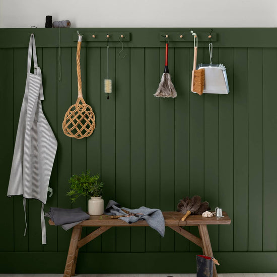 Entrée aux murs vert treillis et blanc grisaille Libéron, avec banc en bois, patères et accessoires ménagers.