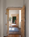 Couloir aux murs vert treillis et crème topinambour Libéron, avec portes en bois, pierre apparente et tapis rayé.