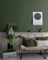 Salon aux murs vert treillis et gris sarrasin Libéron, avec banquette, soubassement gris et plante verte.