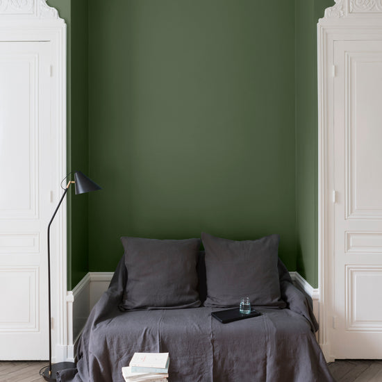 Salon aux murs vert treillis Libéron, avec canapé gris, portes blanches, lampadaire noir et parquet clair.
