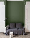Salon aux murs vert treillis Libéron, avec canapé gris, portes blanches, lampadaire noir et parquet clair.
