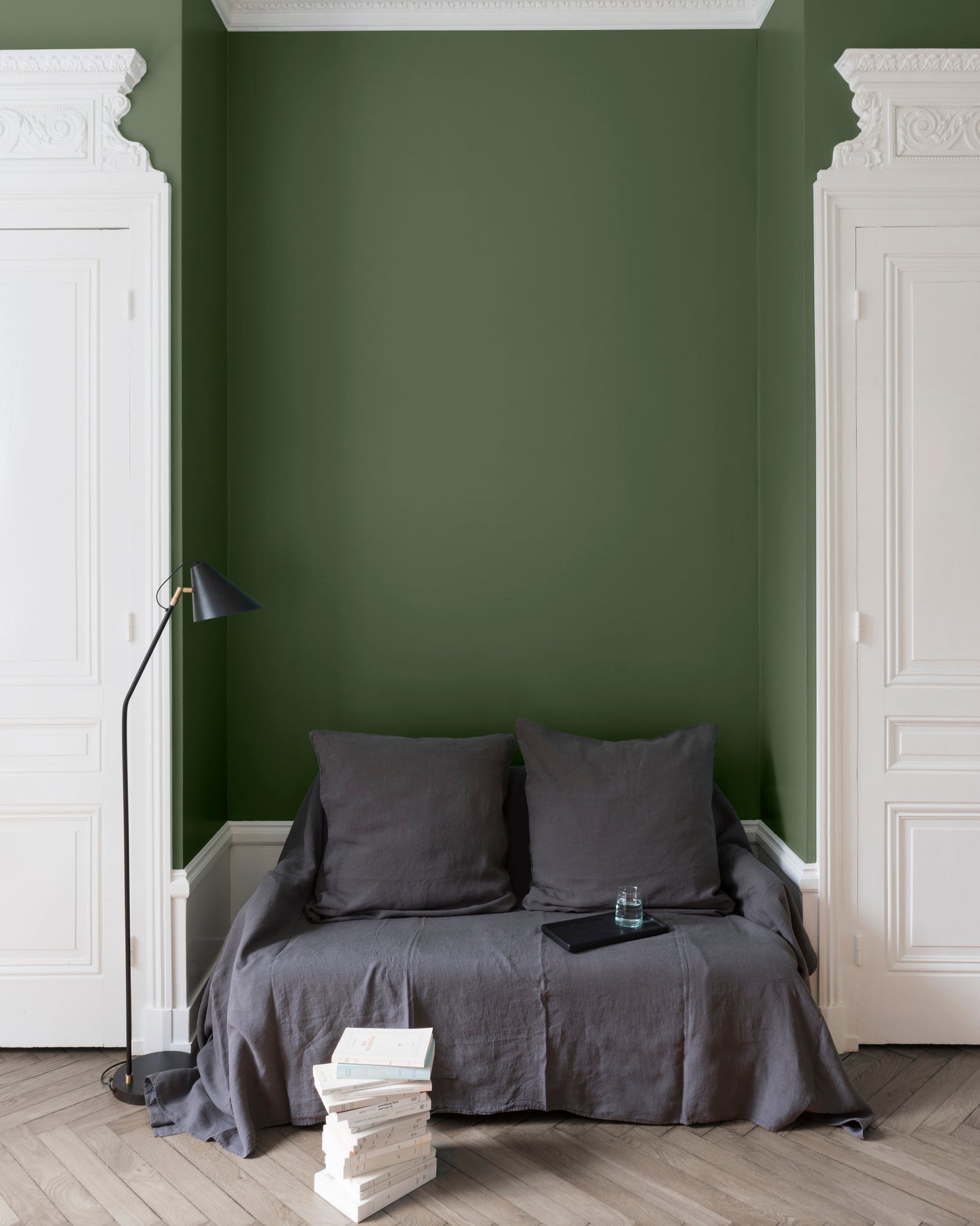 Salon aux murs vert treillis Libéron, avec canapé gris, portes blanches, lampadaire noir et parquet clair.