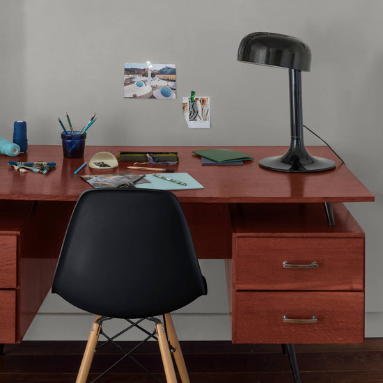 Coin bureau verni avec le Vernis Bistrot Acajou Libéron, chaise et lampe noires, photos accrochées sur le mur gris.