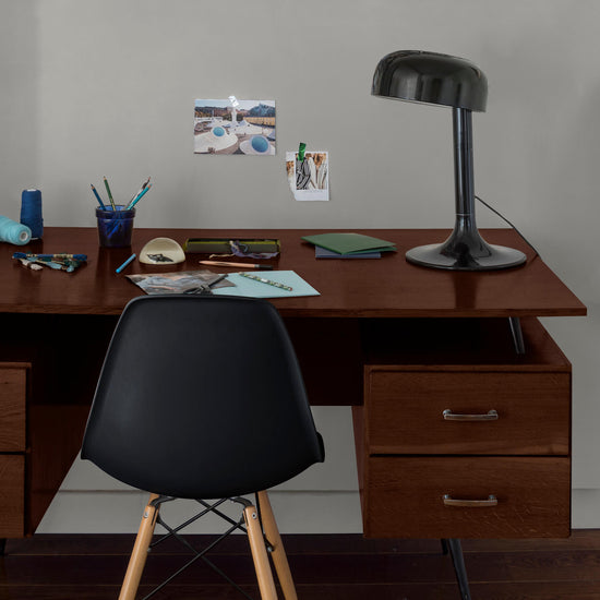 Coin bureau verni avec le Vernis Bistrot Chêne Foncé Libéron, chaise et lampe noires, photos accrochées sur le mur gris.