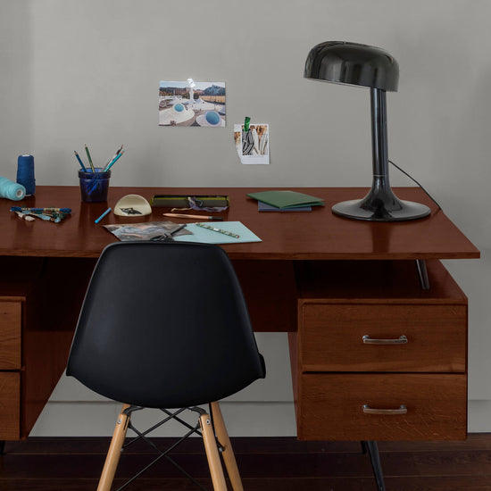 Coin bureau verni avec le Vernis Bistrot Chêne Moyen Libéron, chaise et lampe noires, photos accrochées sur le mur gris.