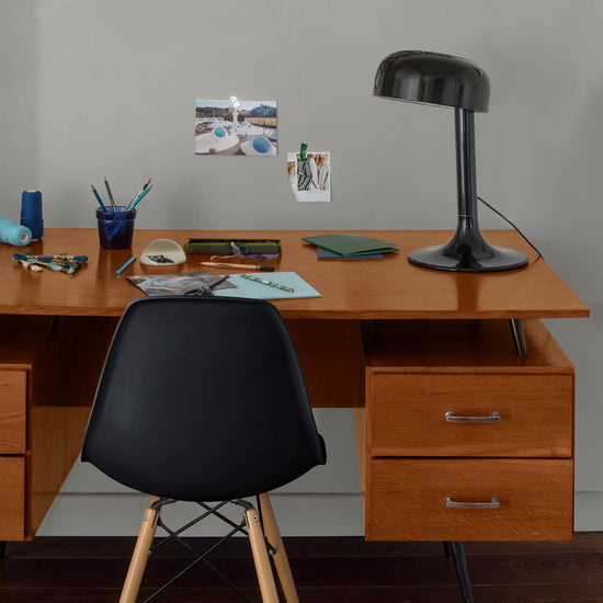 Coin bureau verni avec le Vernis Bistrot Merisier Libéron, chaise et lampe noires, photos accrochées sur le mur gris.