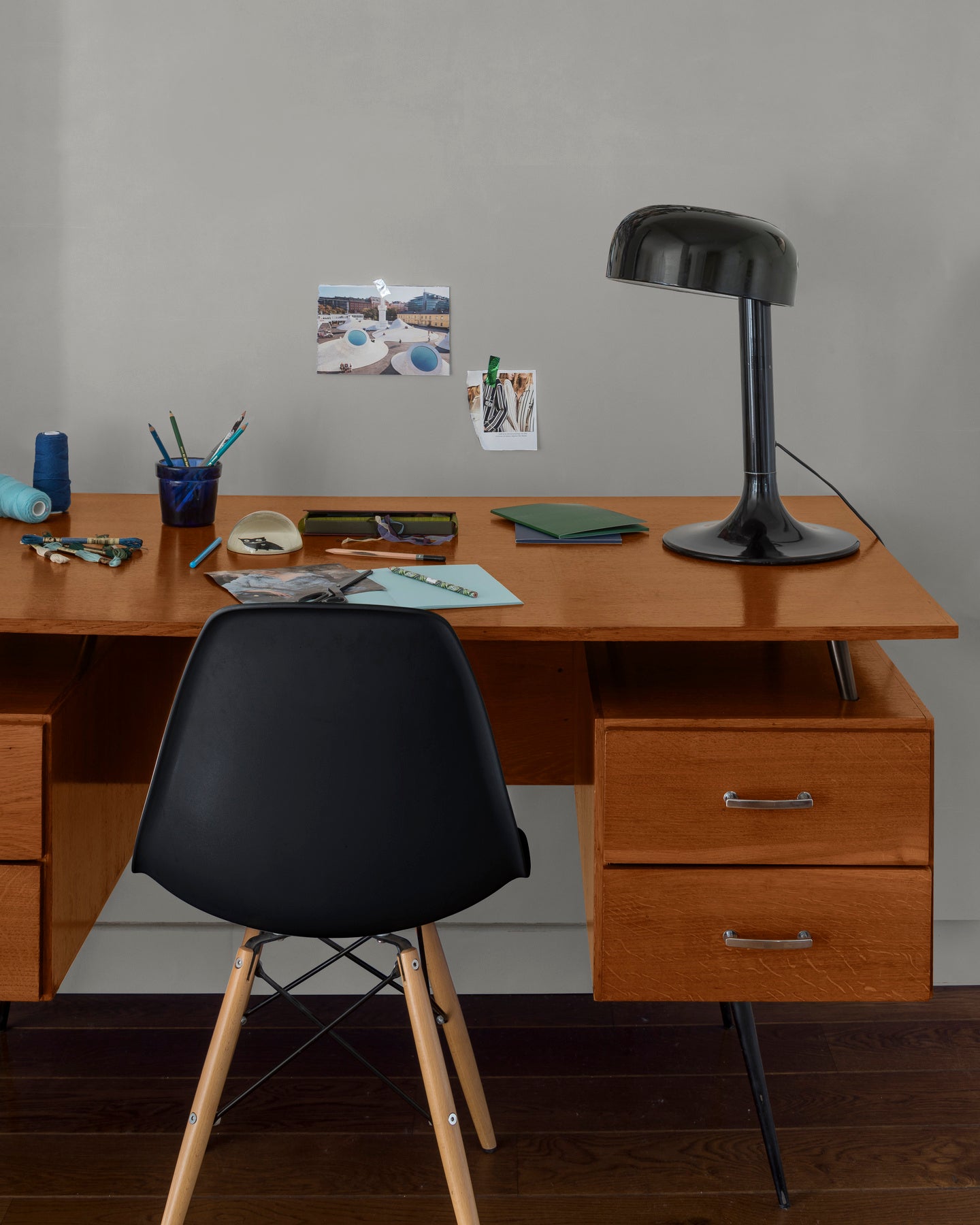 Coin bureau verni avec le Vernis Bistrot Merisier Libéron, chaise et lampe noires, photos accrochées sur le mur gris.
